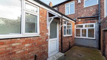 A narrow alleyway with brick houses, a white door, and a window with frosted glass.