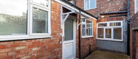 A narrow alleyway with brick houses, a white door, and a window with frosted glass.