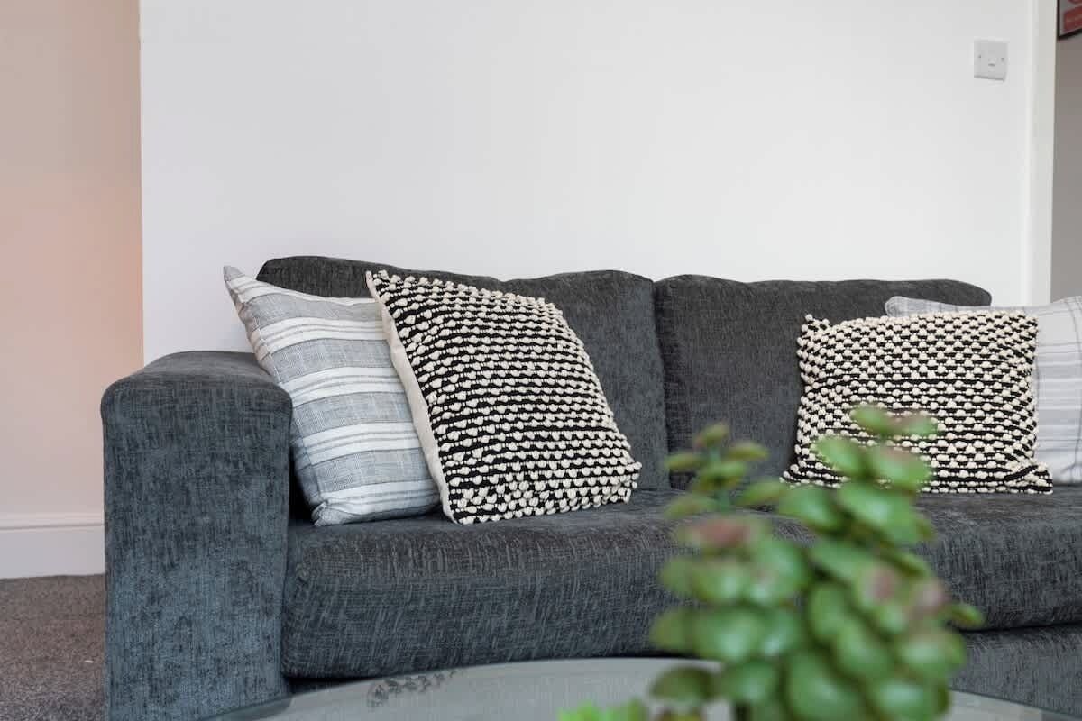 A grey sofa with three patterned cushions against a plain wall.