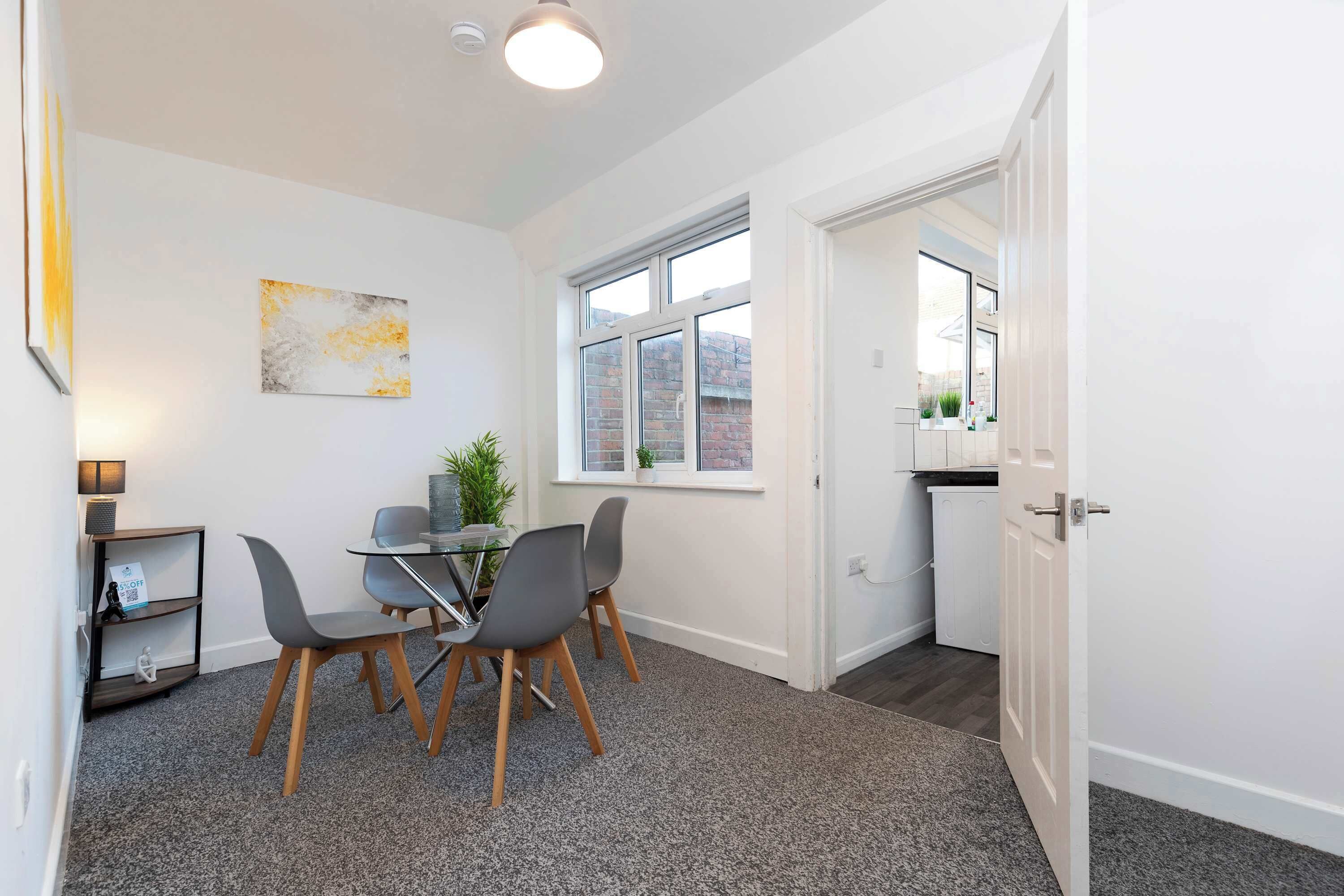 A modern room with a dining area, a window with a view of a brick building, and a door leading to a kitchen.