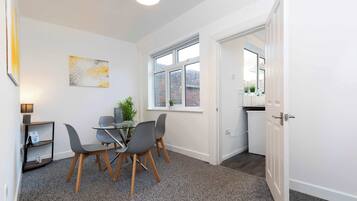 A modern room with a dining area, a window with a view of a brick building, and a door leading to a kitchen.