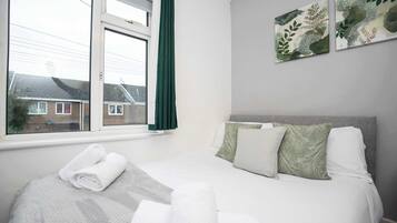 A neatly made bed with pillows and a rolled towel, a window with curtains, and a wall with framed artwork.