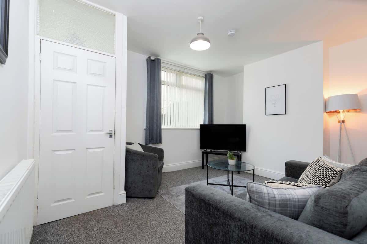 A modern living room with a grey sofa, a small coffee table, a flat-screen TV, and a lamp.