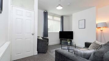 A modern living room with a grey sofa, a small coffee table, a flat-screen TV, and a lamp.