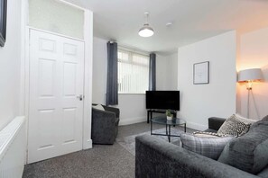 A modern living room with a grey sofa, a small coffee table, a flat-screen TV, and a lamp.
