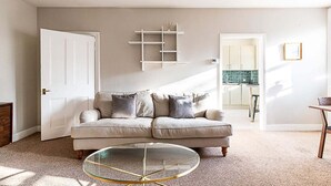 A living room with a beige sofa, a glass coffee table, and a white door. - Beautiful One-Bedroom Apartment In Notting Hill (London)