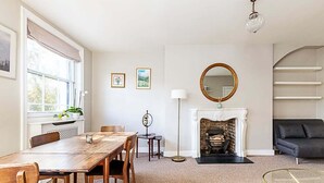 A room with a wooden dining table, chairs, a fireplace, a sofa, and a round mirror. - Beautiful One-Bedroom Apartment In Notting Hill (London)