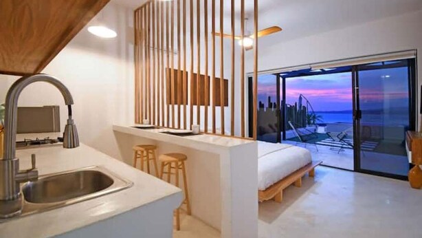 A modern kitchen with a built-in sink, wooden stools, and a view of the ocean through a glass door. - Unique Unit-Private Pool,Isla Espiritu Santo VIEW! (La Paz)