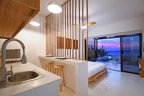 A modern kitchen with a built-in sink, wooden stools, and a view of the ocean through a glass door.