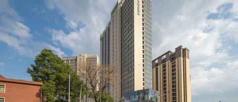 Un edificio alto con varios pisos, rodeado de otros edificios y árboles.