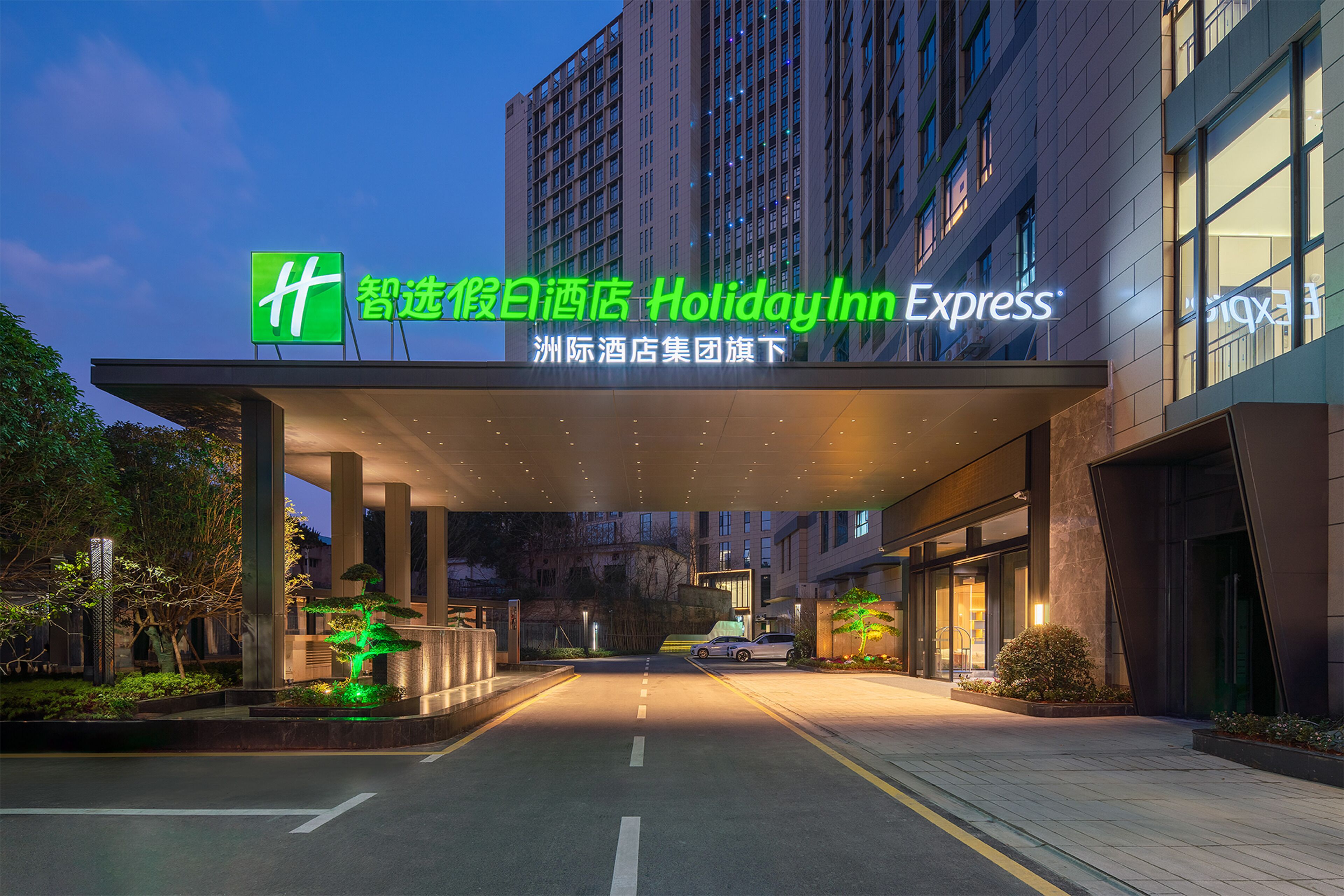 A Holiday Inn Express hotel entrance with a covered walkway, illuminated signage, and a parking area.
