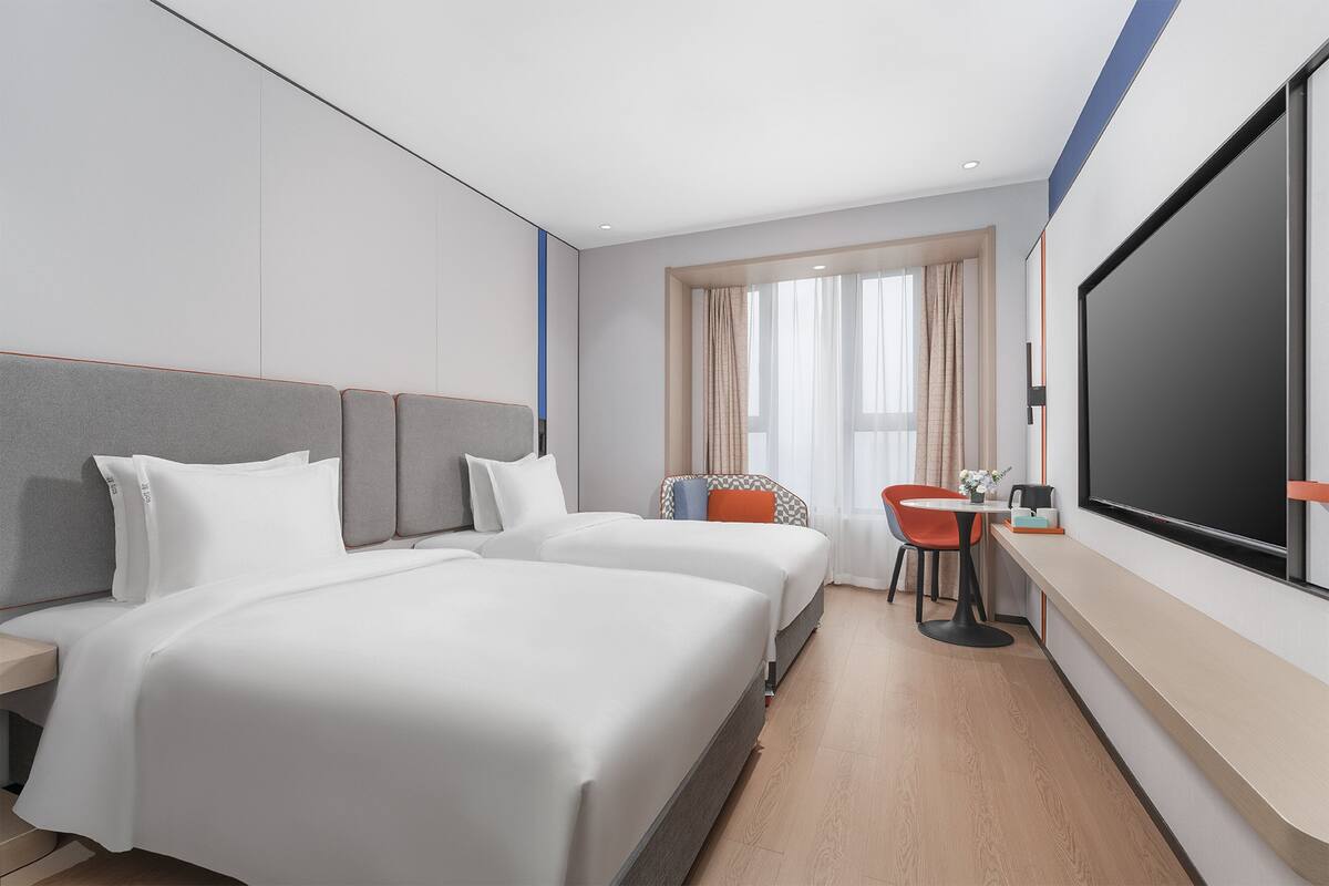Ein Hotelzimmer mit zwei Betten, einem Schreibtisch, einem Stuhl, einem Fernseher und einem Fenster mit Vorhängen.