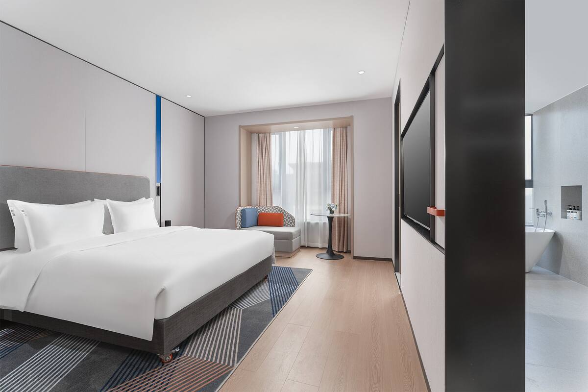 Ein modernes Hotelzimmer mit einem großen Bett, einer Sitzecke mit Tisch und einem separaten Badezimmer.