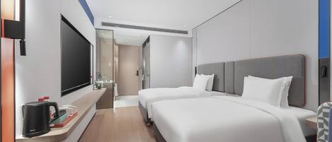 Habitación de hotel con dos camas, televisión, cafetera y baño visible a través de una puerta de vidrio.