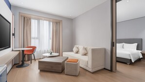 A modern hotel room with a sofa, ottoman, coffee table, and a TV on a desk. - Holiday Inn Express Changsha Yuhua by IHG (Changsha)