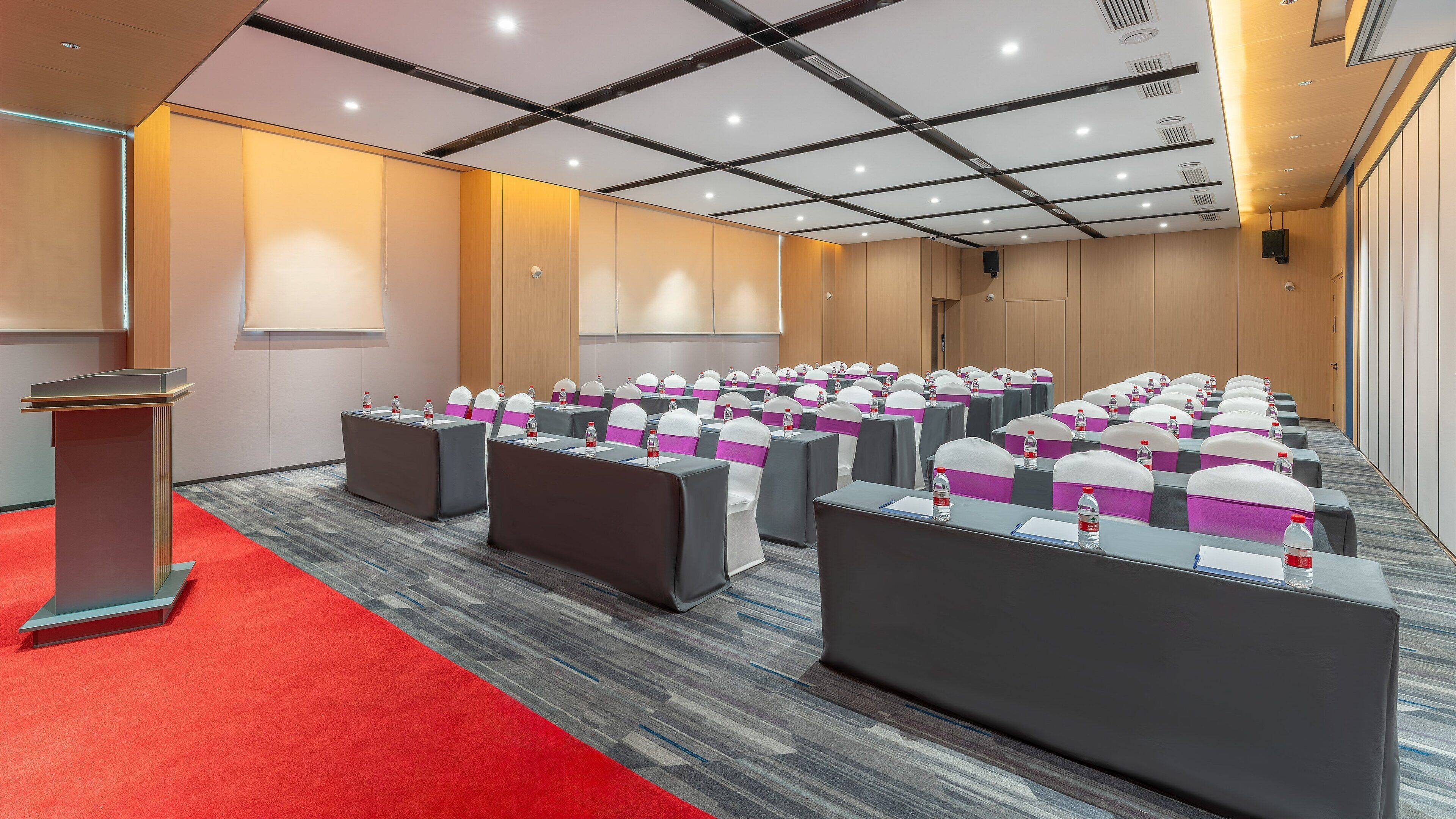 Un salón de conferencias con filas de mesas, cada una con una botella de agua y un portanombres.
