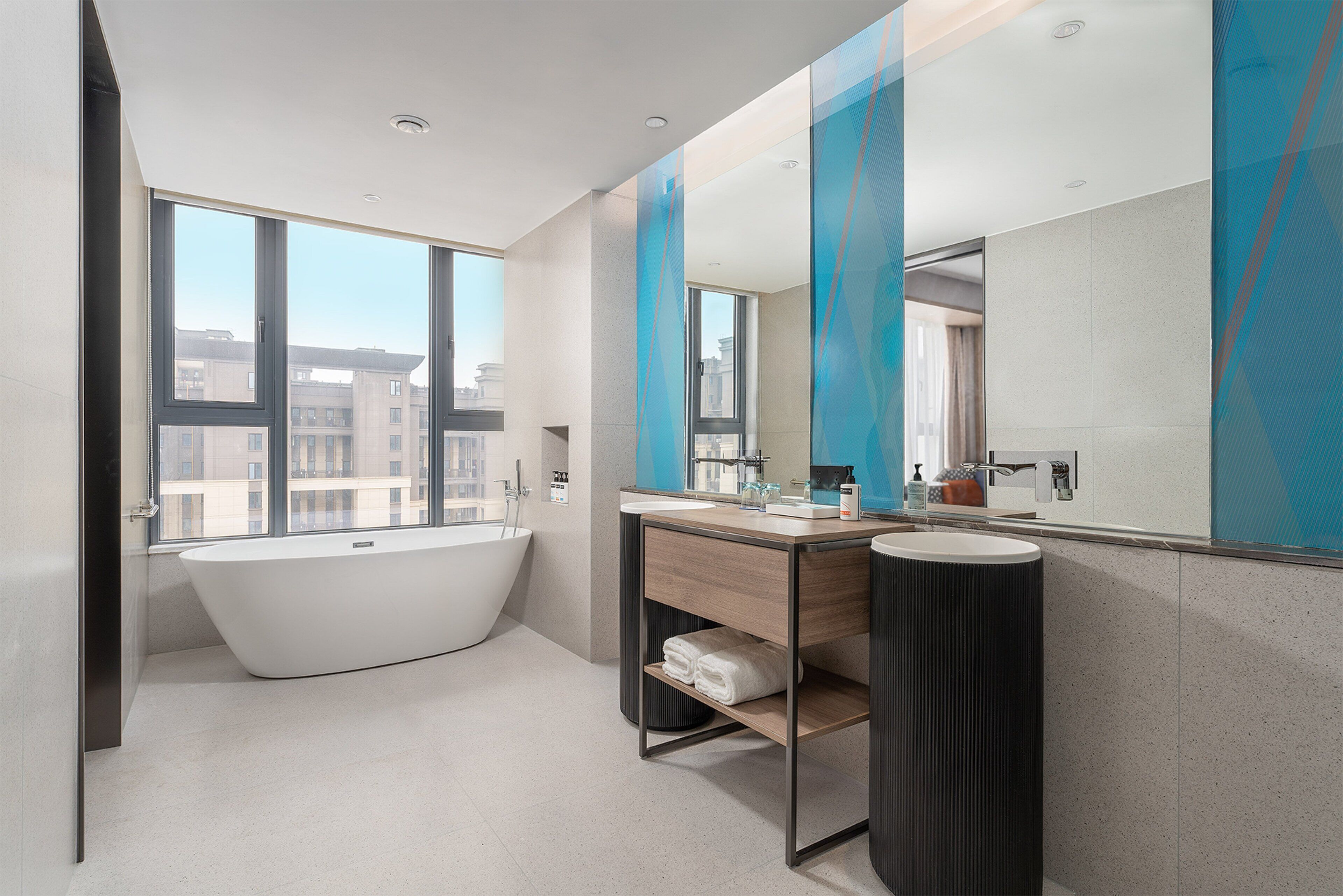 Une salle de bain moderne avec une baignoire sur pieds, un meuble-lavabo avec un miroir et une grande fenêtre donnant sur la ville.
