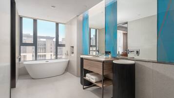 A modern bathroom with a freestanding bathtub, a vanity with a mirror, and a large window offering a city view.