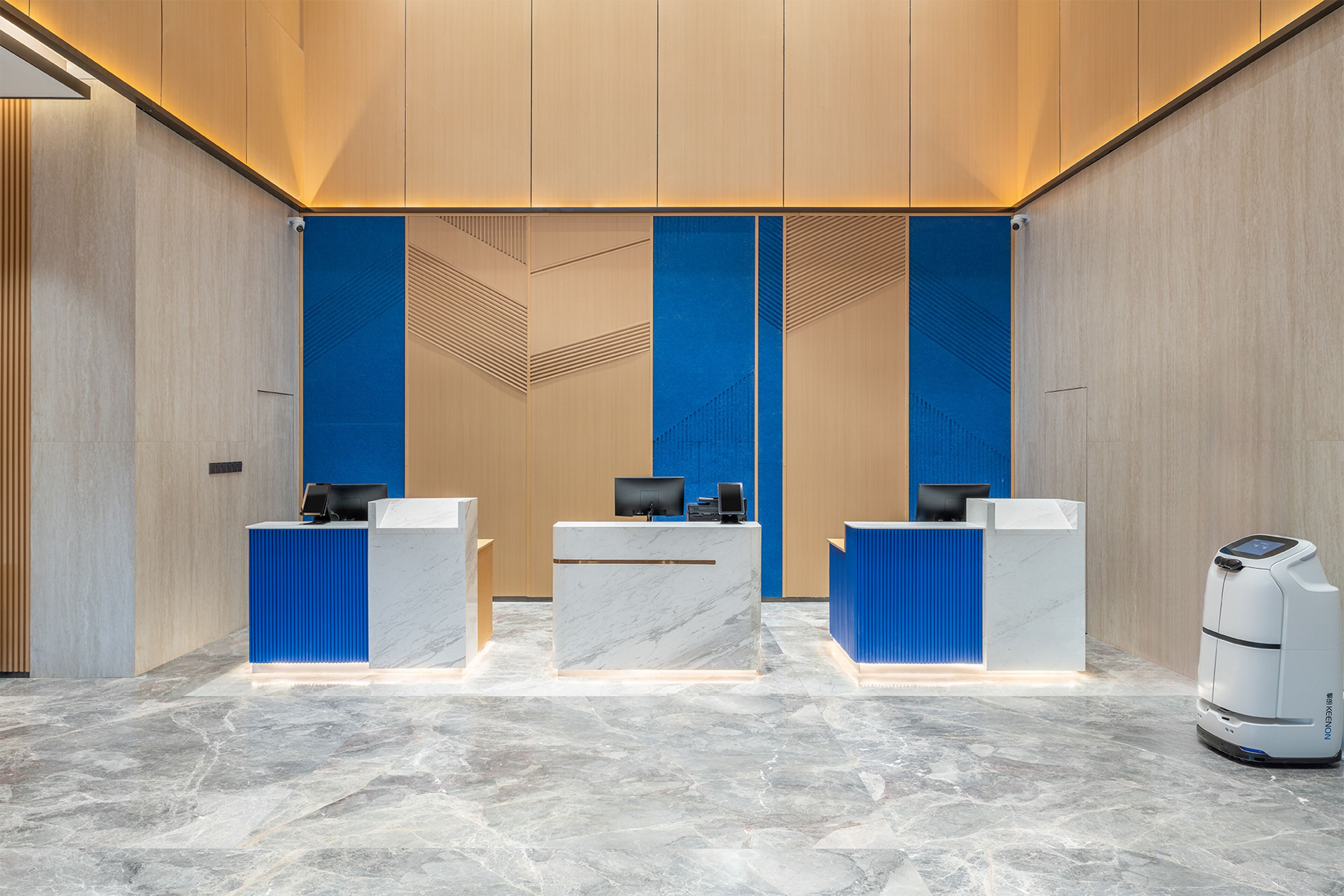 A reception area with three counters, each with a computer and a chair. The walls are wooden, and the floor is marble.