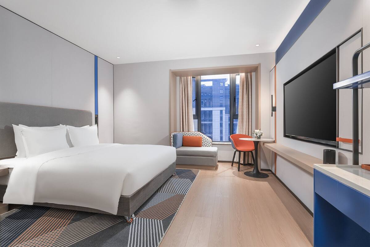 Ein modernes Hotelzimmer mit einem großen Bett, einem Schreibtisch, einem Sessel und einem Fernseher.