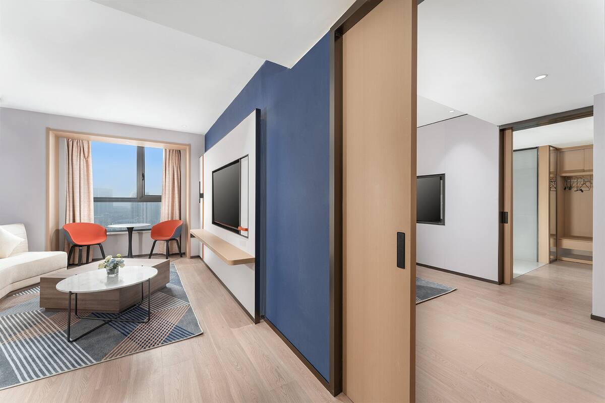 Ein modernes Hotelzimmer mit einer Couch, zwei Sesseln, einem Fernseher und einem großen Fenster.