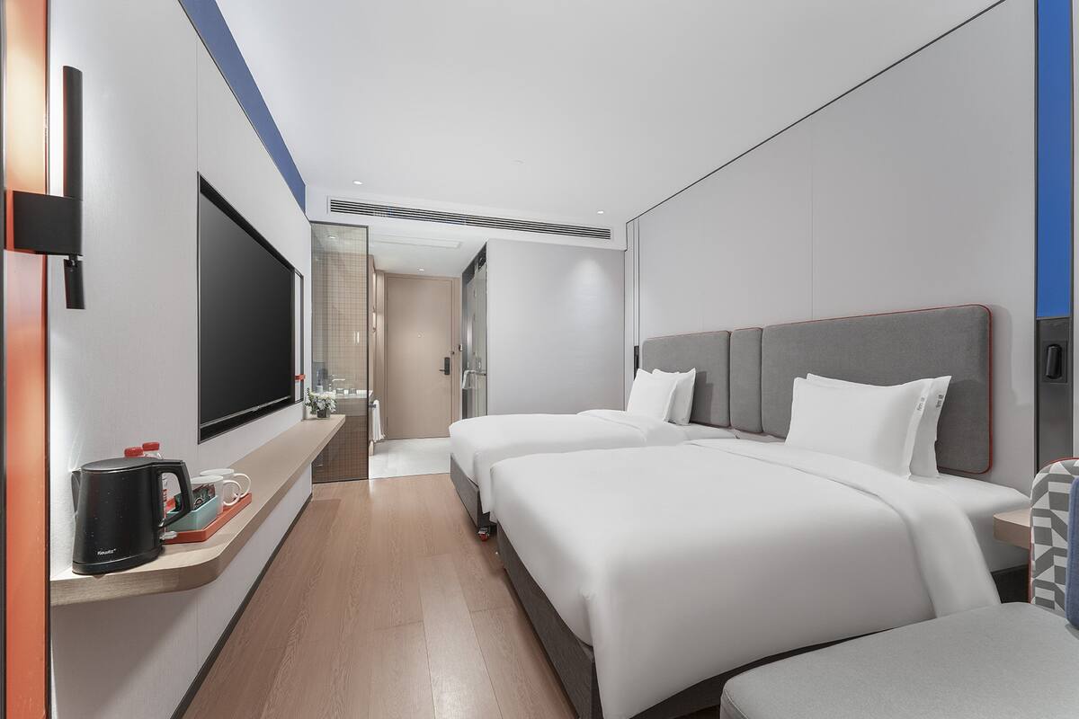 Ein modernes Hotelzimmer mit zwei Betten, einem Flachbildfernseher, einer Kaffeemaschine und einem kleinen Tisch mit Tablett.