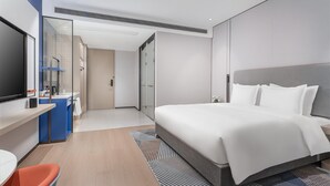 A modern hotel room with a large bed, a desk with a flat-screen TV, a bathroom with a glass shower enclosure, and a small seating area with a chair. - Holiday Inn Express Changsha Yuhua by IHG (Changsha)
