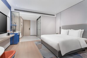 A modern hotel room with a large bed, a desk with a flat-screen TV, a bathroom with a glass shower enclosure, and a small seating area with a chair. - Holiday Inn Express Changsha Yuhua by IHG (Changsha)