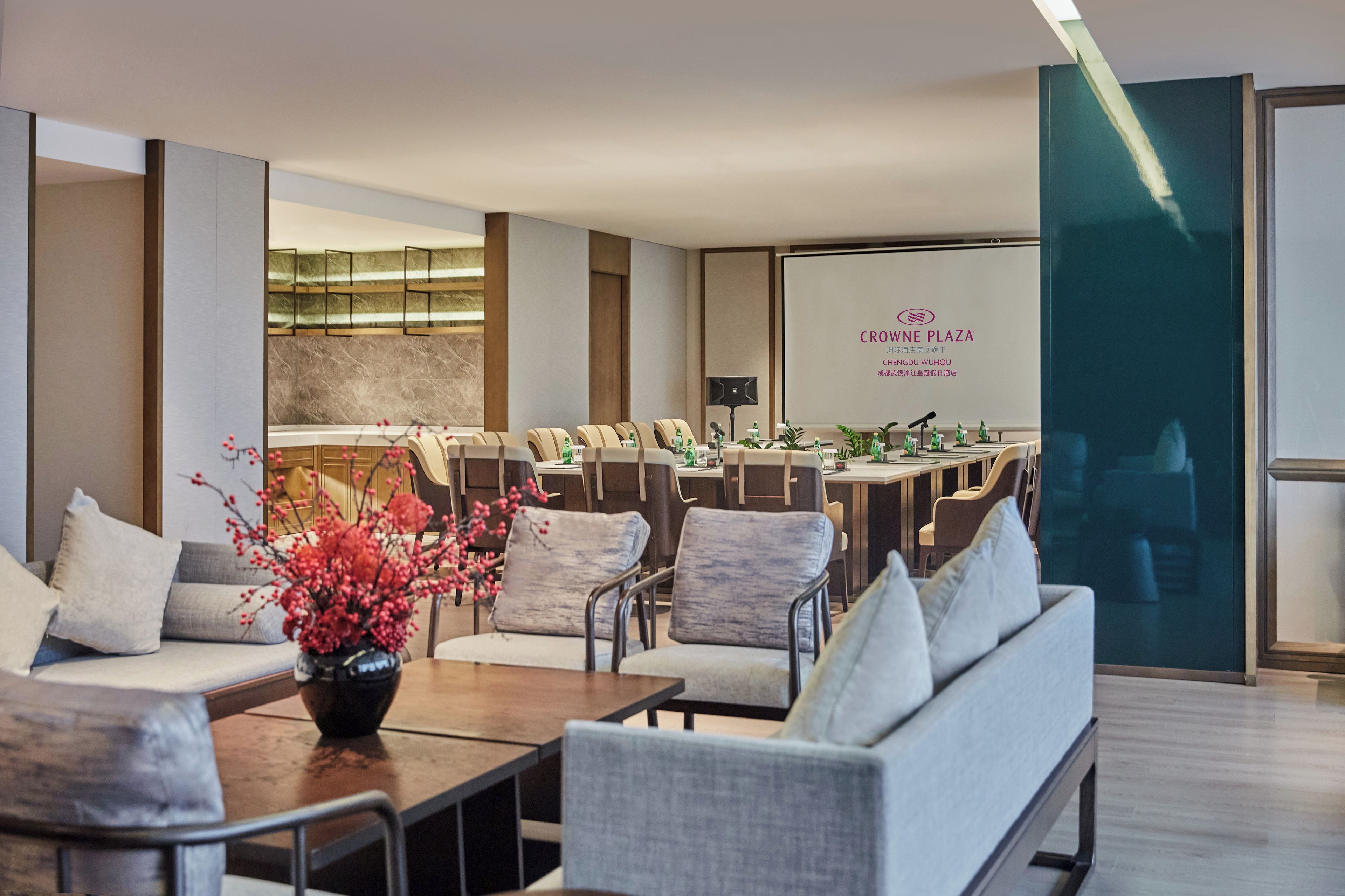 Un vestíbul d'hotel modern amb zones d'estar, una recepció i una gran pantalla que mostra el nom de l'hotel.