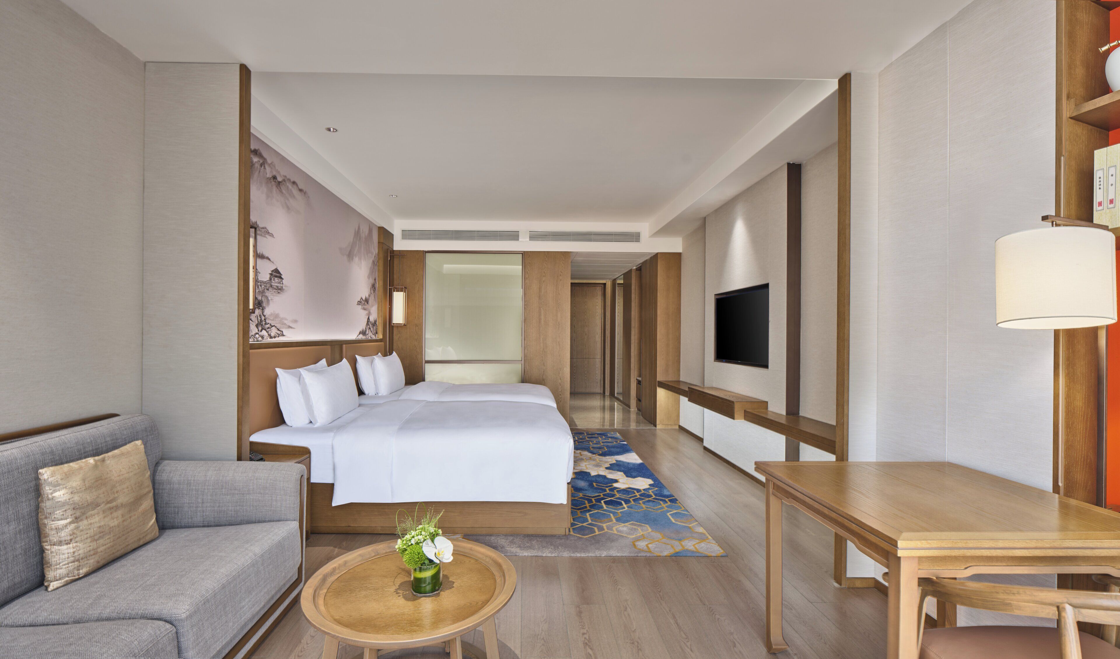 A hotel room with a bed, a sofa, a table, a TV, and a decorative wall.