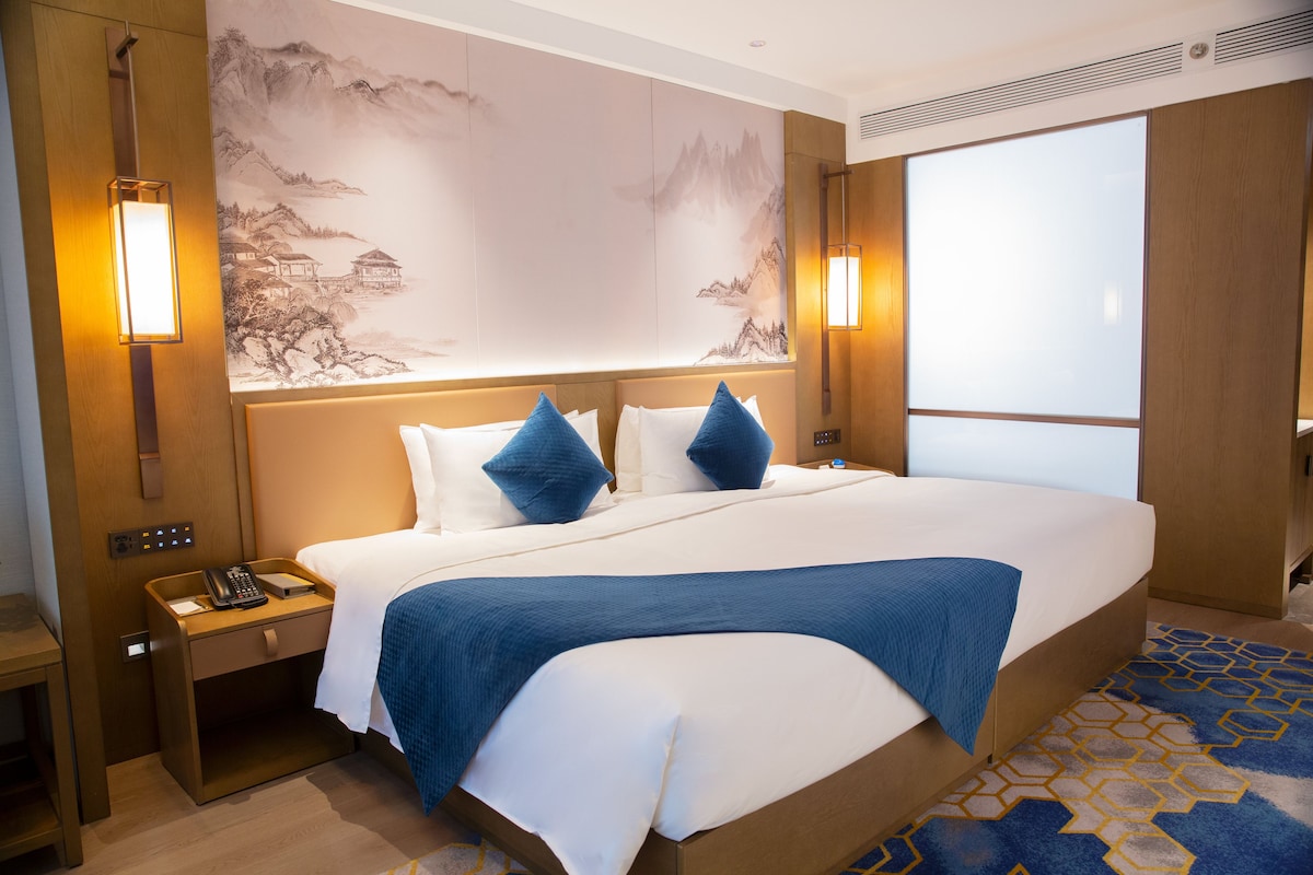 Een hotelkamer met een groot bed, twee nachtkastjes, een wandlamp en een groot raam.