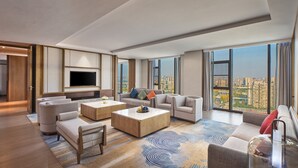 Amplia sala de estar con un televisor de pantalla plana grande, múltiples opciones de asiento y vista a la ciudad a través de ventanas amplias.