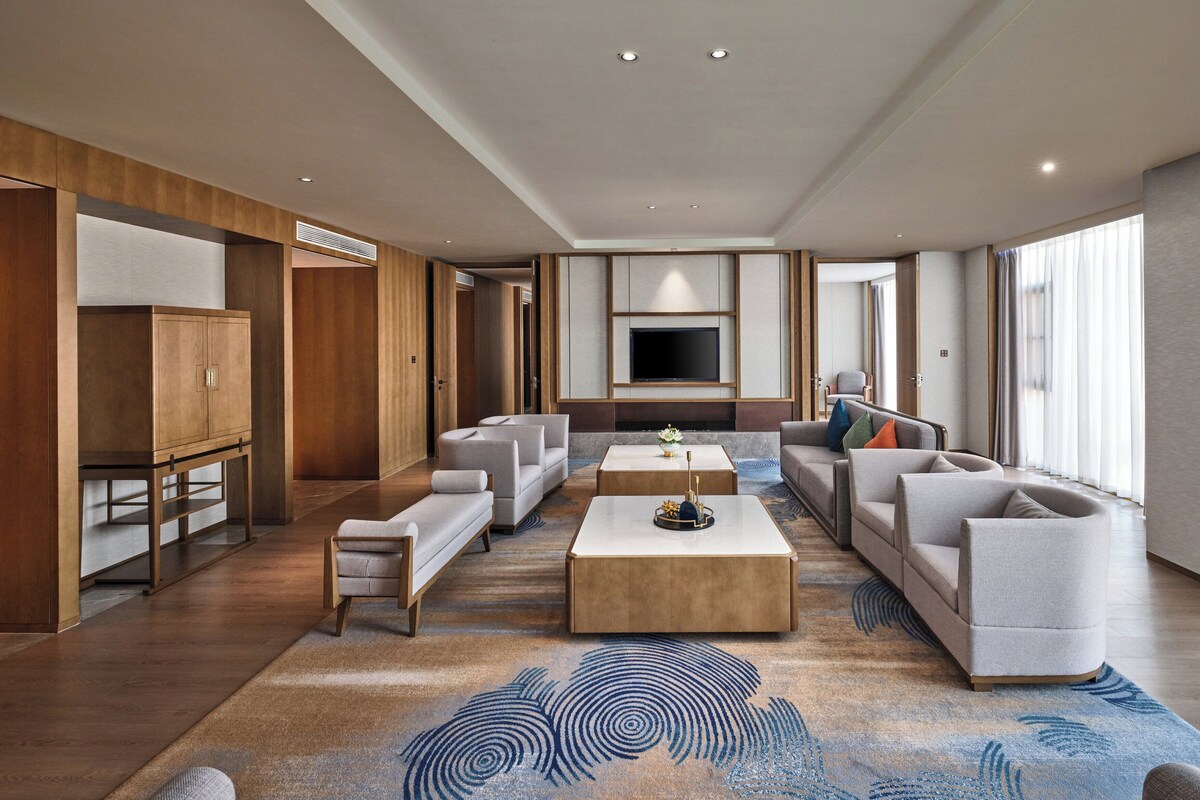 A spacious living room with a large flat-screen TV, multiple seating areas, and a patterned rug.