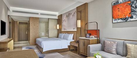 A modern hotel room with a bed, a sofa, a coffee table, and a desk.