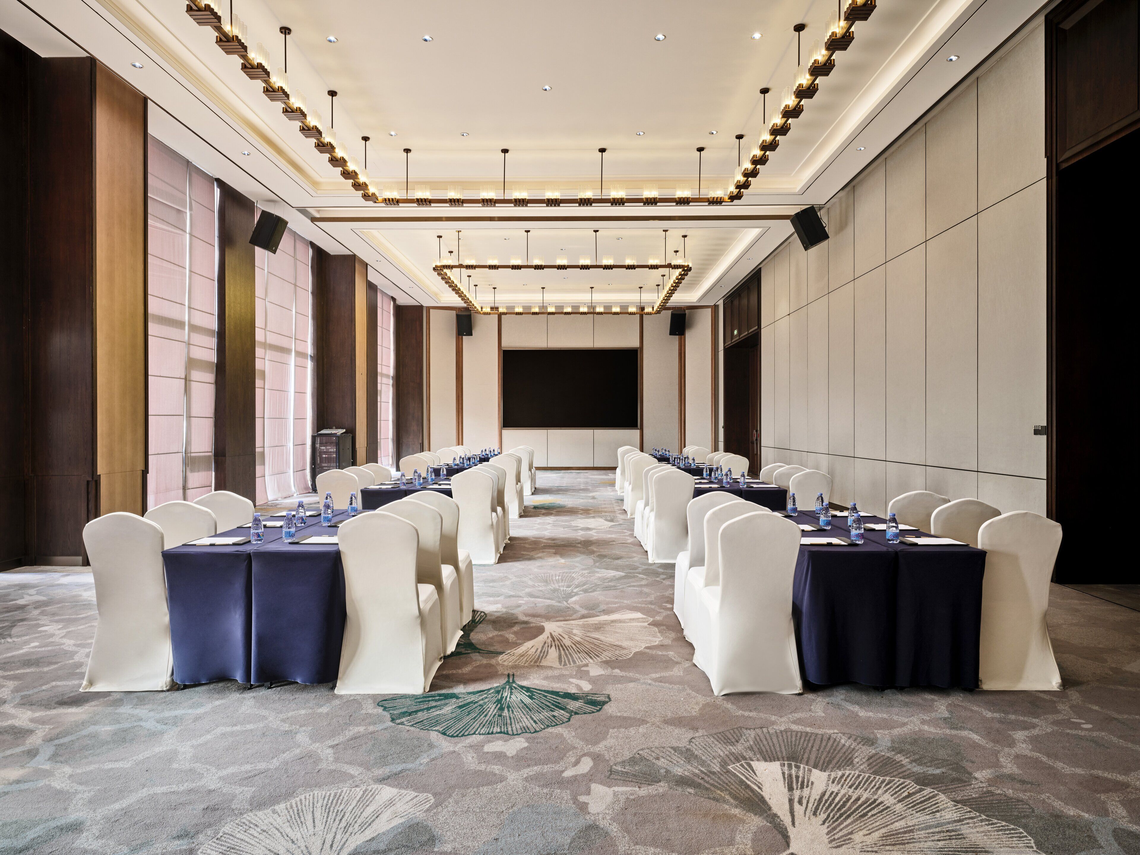 A conference room with a long table, white chairs, and a carpeted floor.