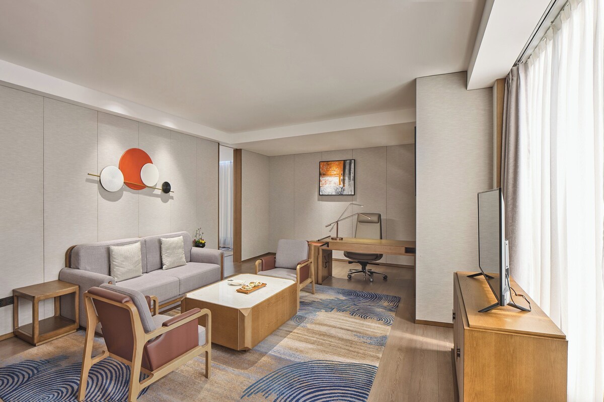 A modern hotel room with a sofa, chairs, a desk, and a flat-screen TV.