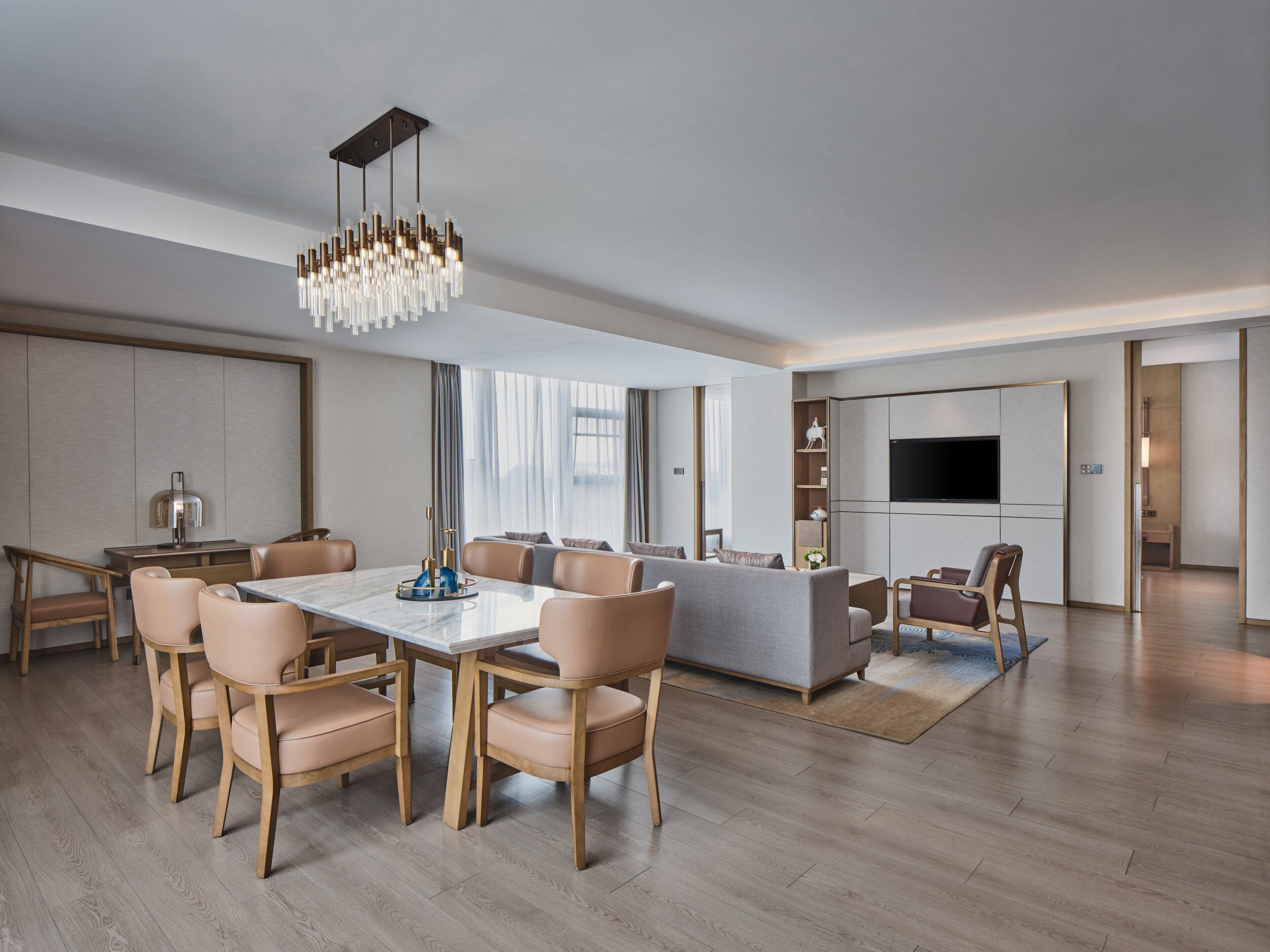 A modern living room with a dining area, wooden flooring, a large TV, and a chandelier.