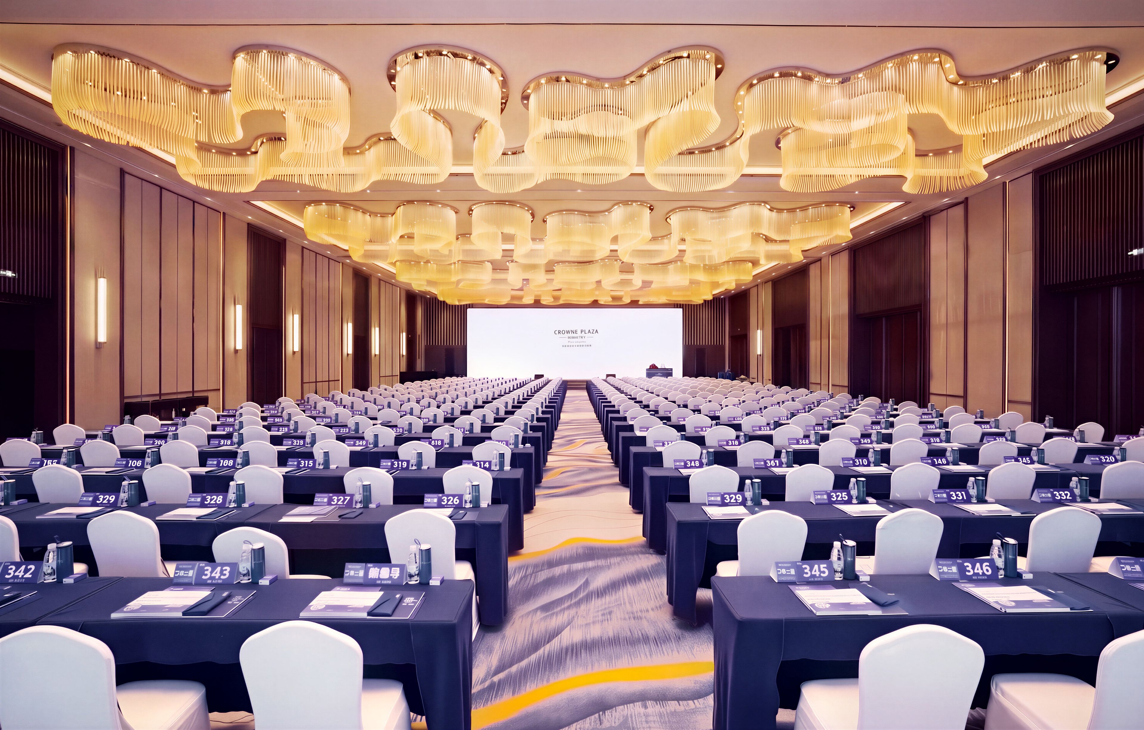 A conference room with rows of tables, chairs, and a large screen at the front.