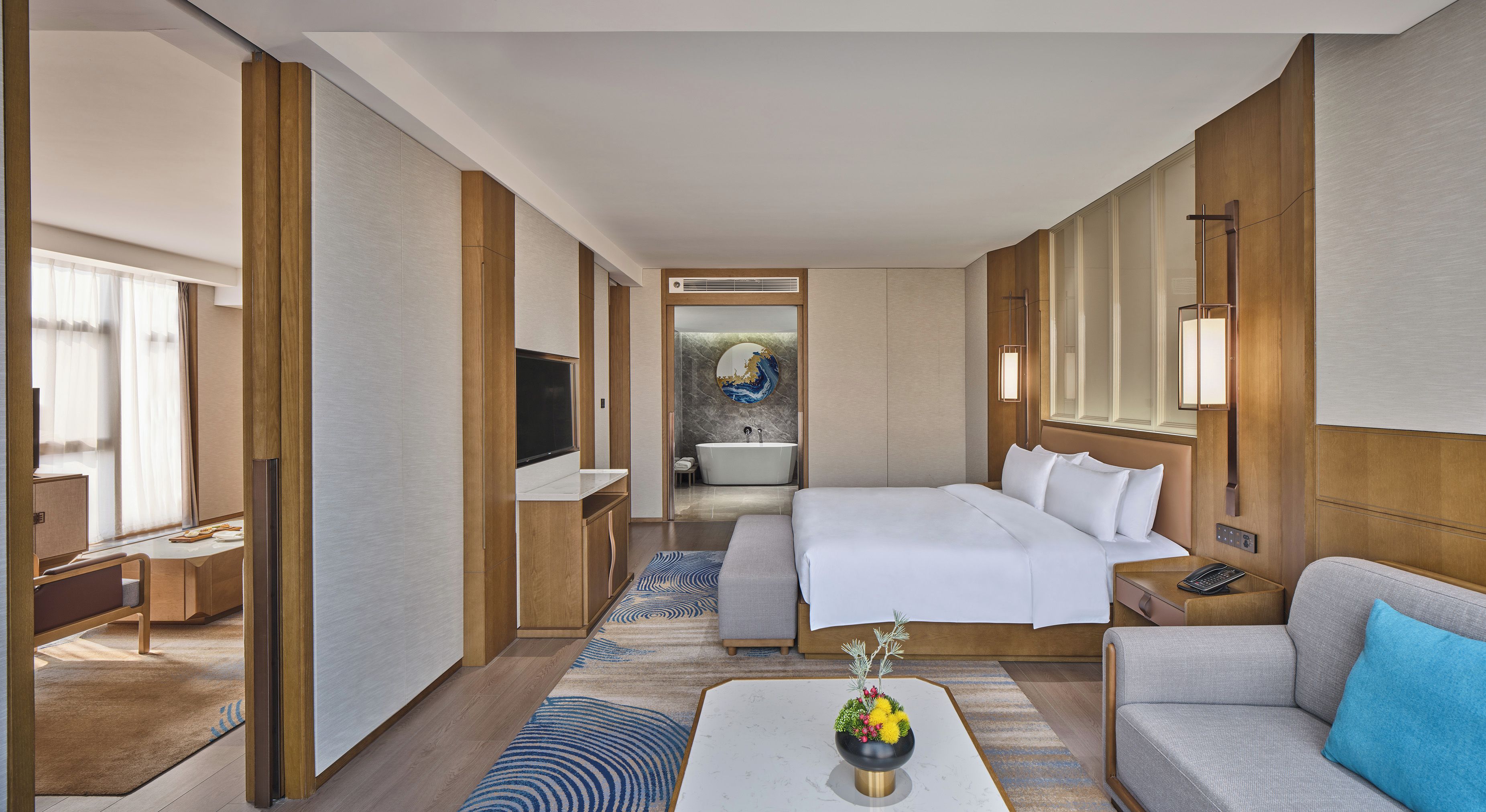 Habitación de hotel con una cama grande, un sofá, un escritorio y un baño visible a través de una puerta abierta.