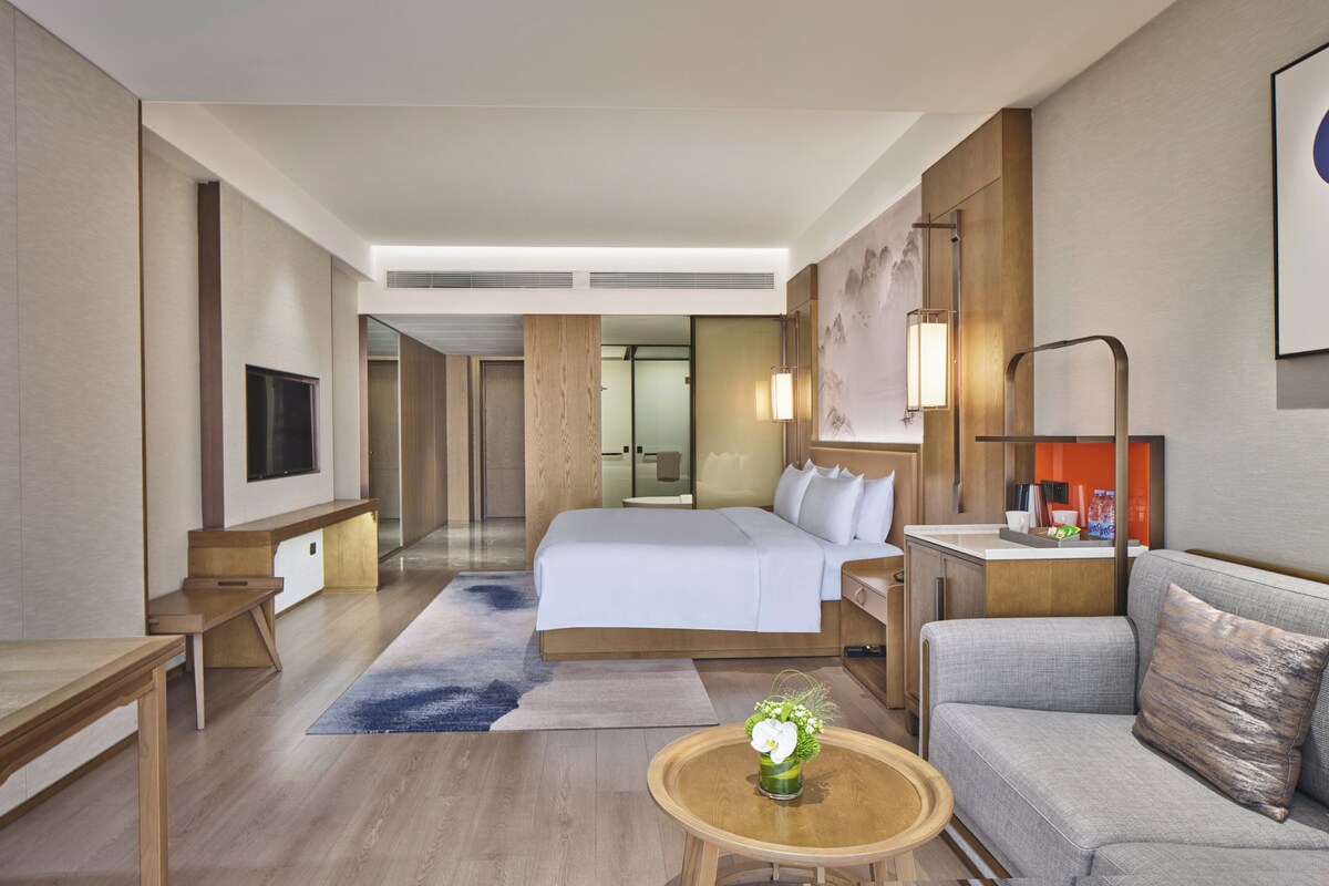 A modern hotel room with a large bed, a sofa, a desk, and a TV.