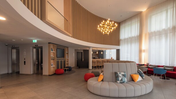 Een moderne hotellobby met een gebogen zithoek, een bar en een televisiescherm.