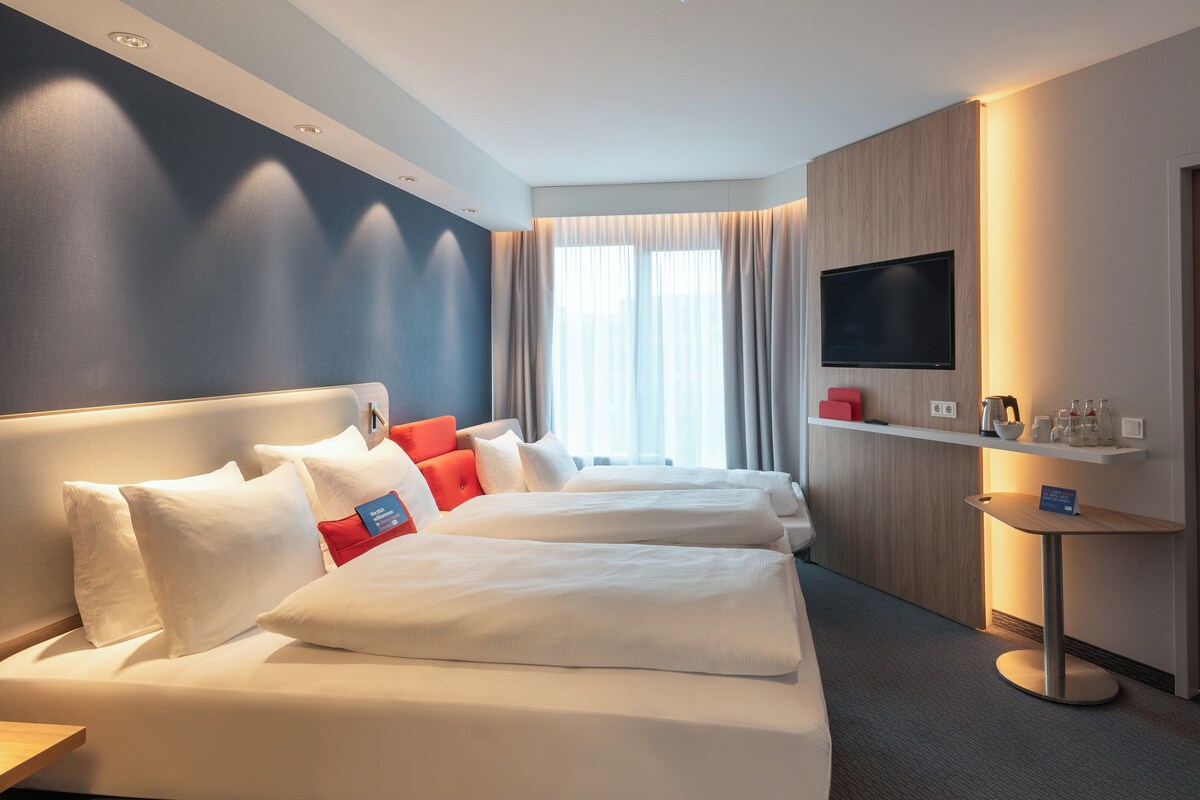 Une chambre d’hôtel avec deux lits, une télévision, un minibar et une porte.