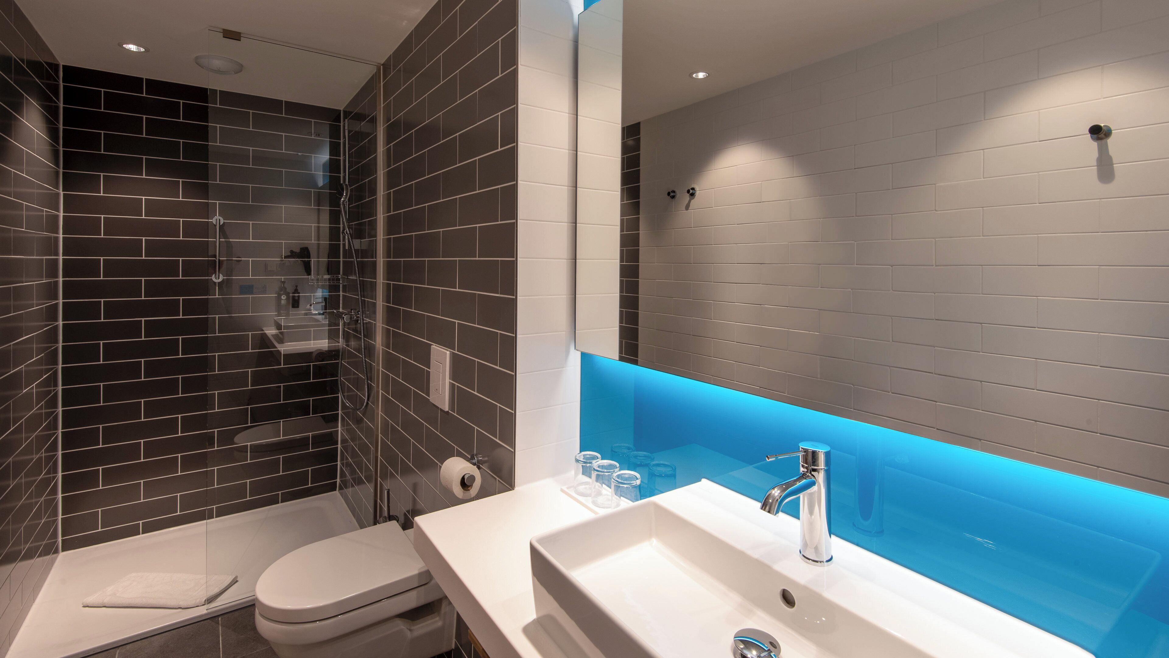 A modern bathroom with a glass-enclosed shower, a white sink with a blue-lit vanity, and a toilet.