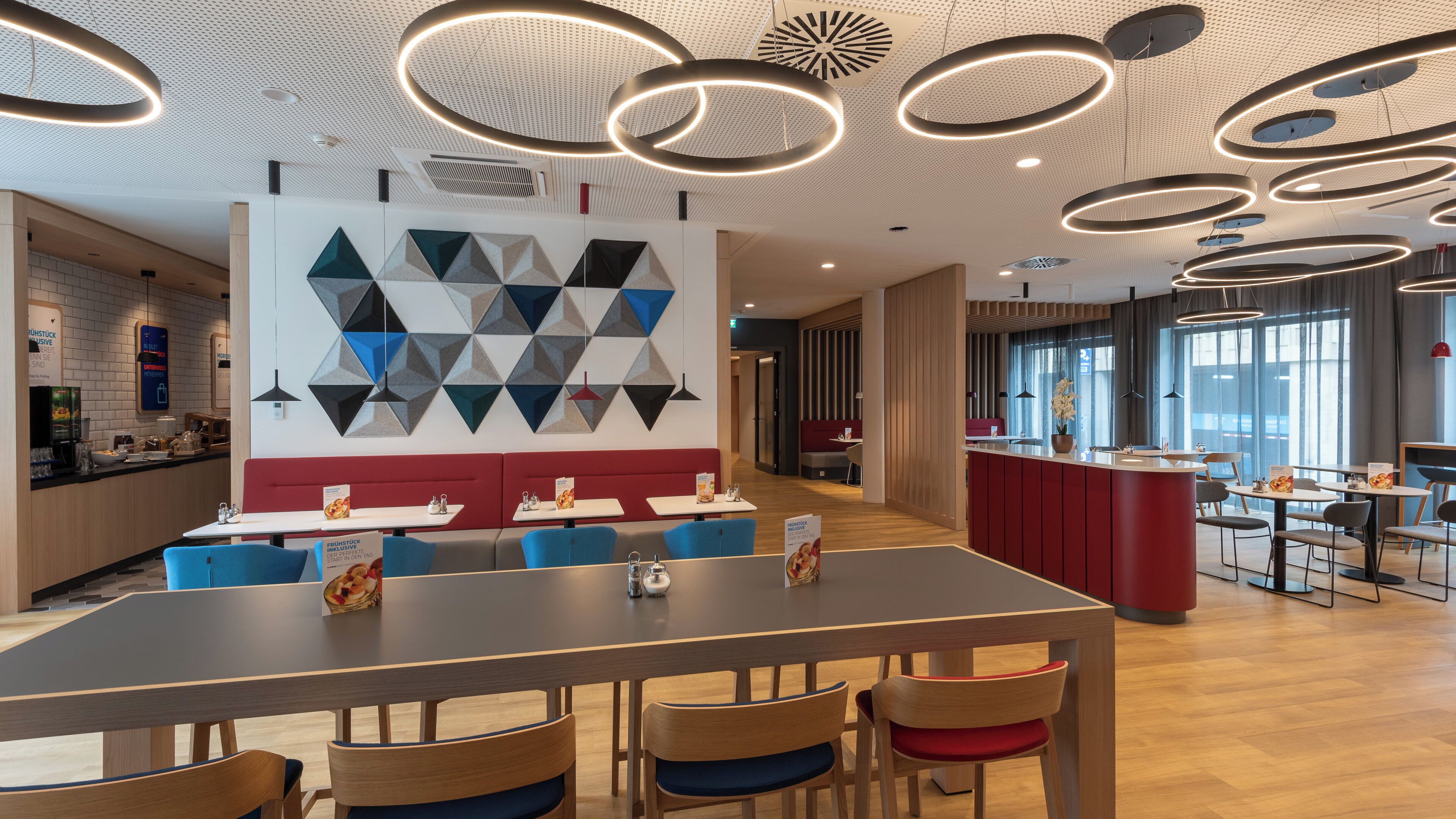 A modern restaurant with a long communal table, booths, and a high ceiling with circular light fixtures.