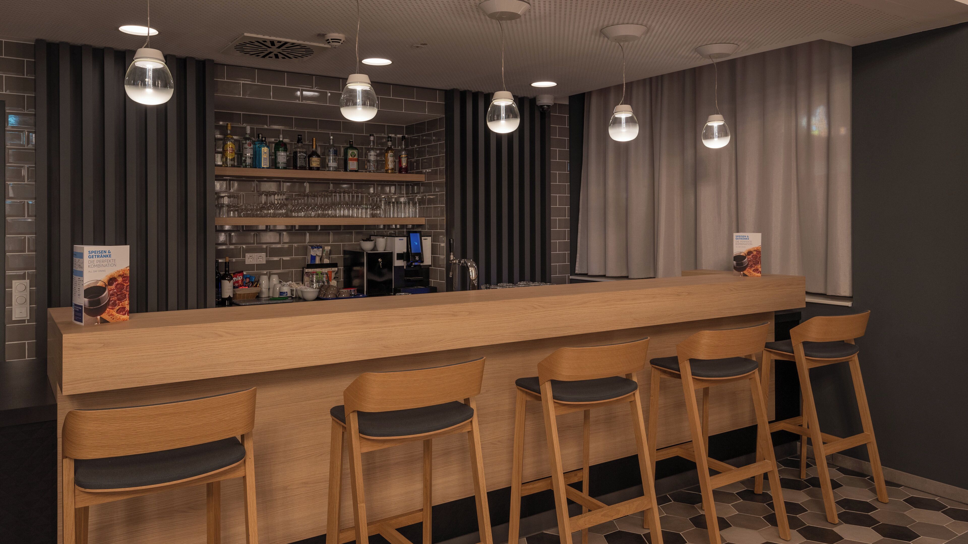 A bar area with a long counter, multiple stools, and a shelf stocked with bottles and glasses.