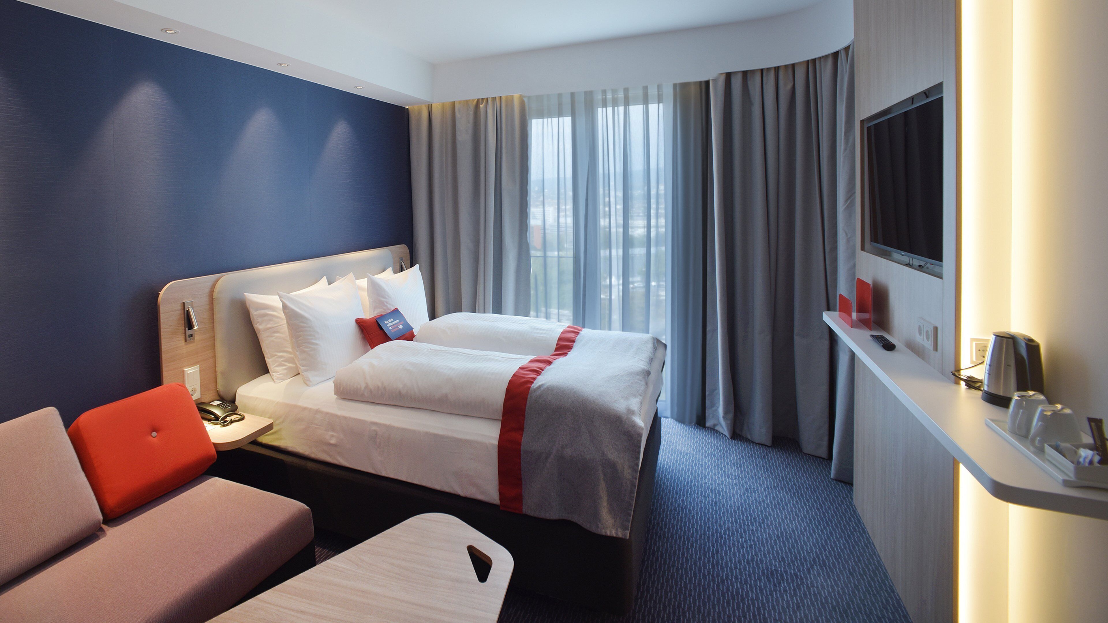 A hotel room with a bed, a desk, a chair, and a TV.
