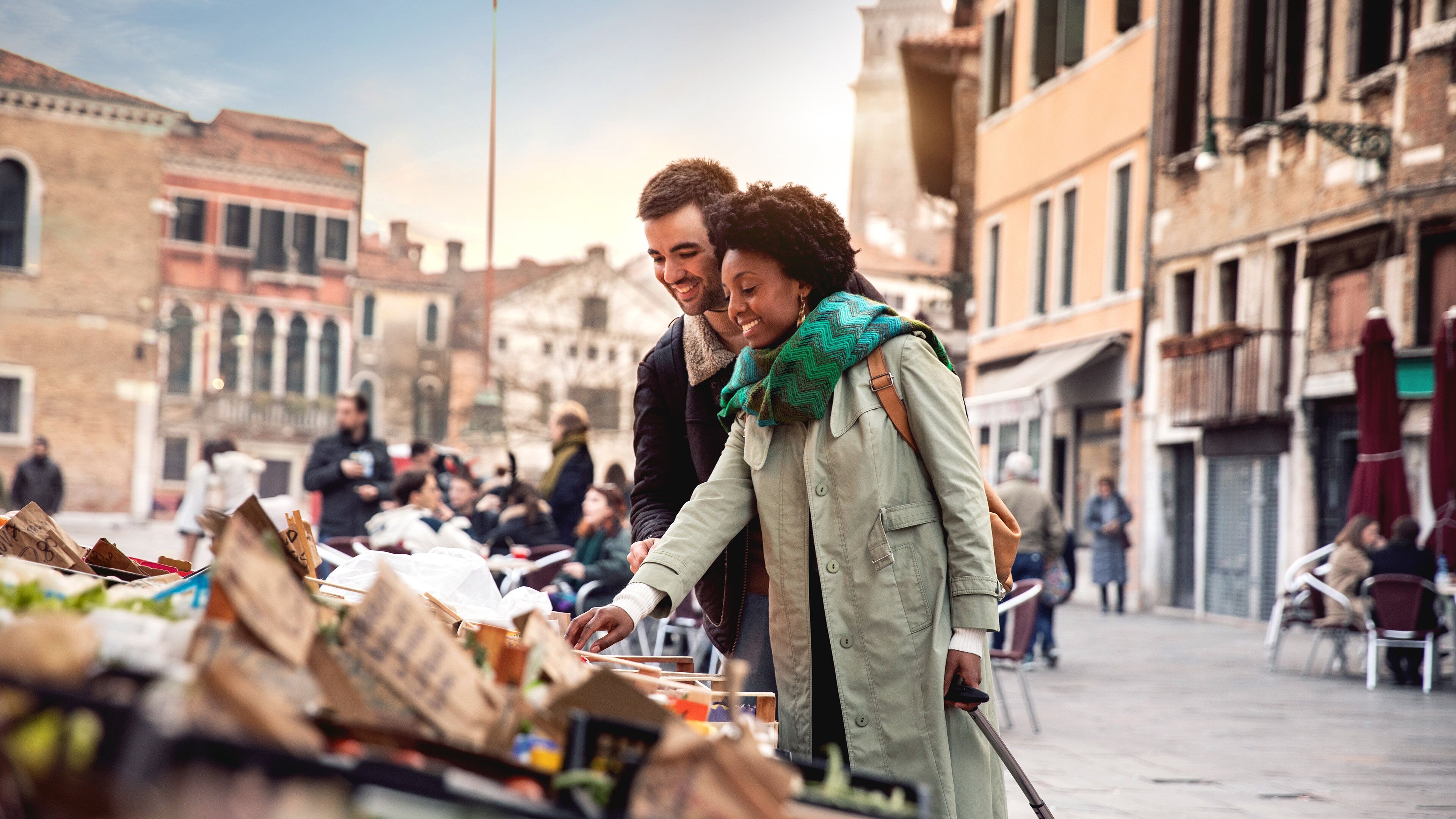 A couple at a street market with various stalls, surrounded by historic buildings.