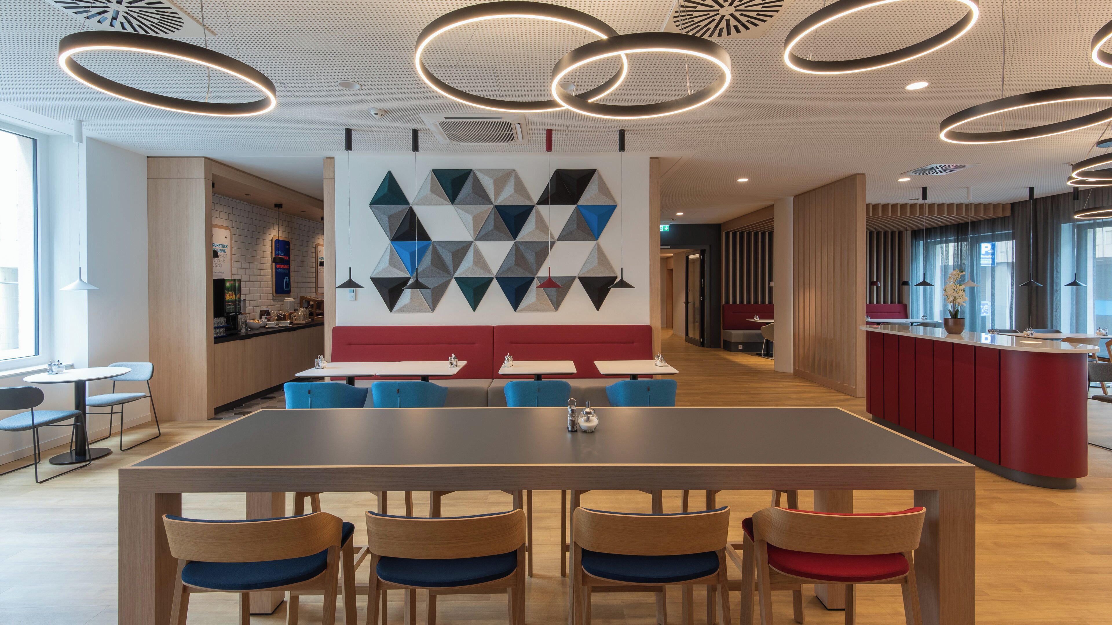 A modern dining area with a long table and chairs, a geometric wall art, and a ceiling with circular light fixtures.