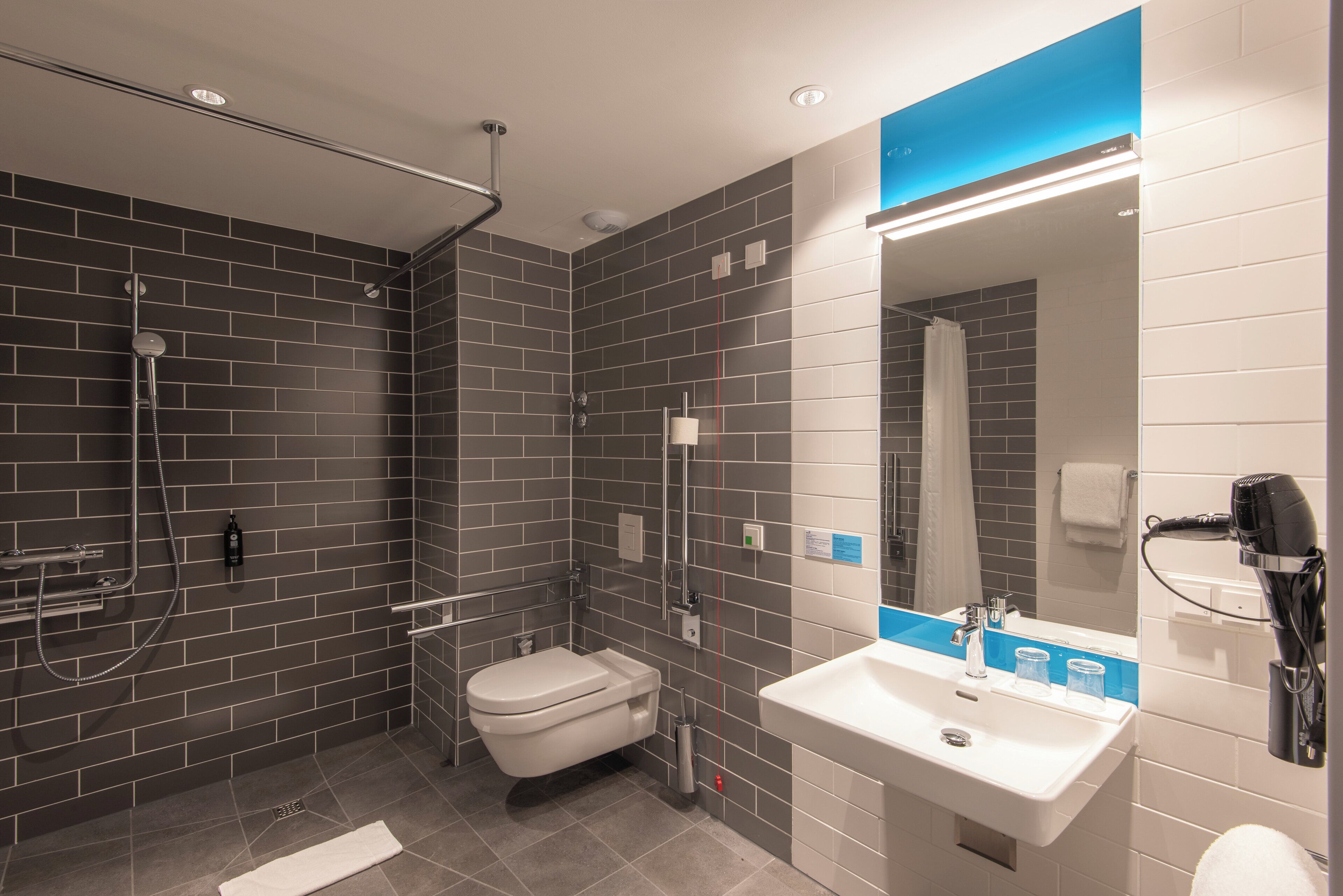 A modern bathroom with a shower, toilet, sink, and a hairdryer.