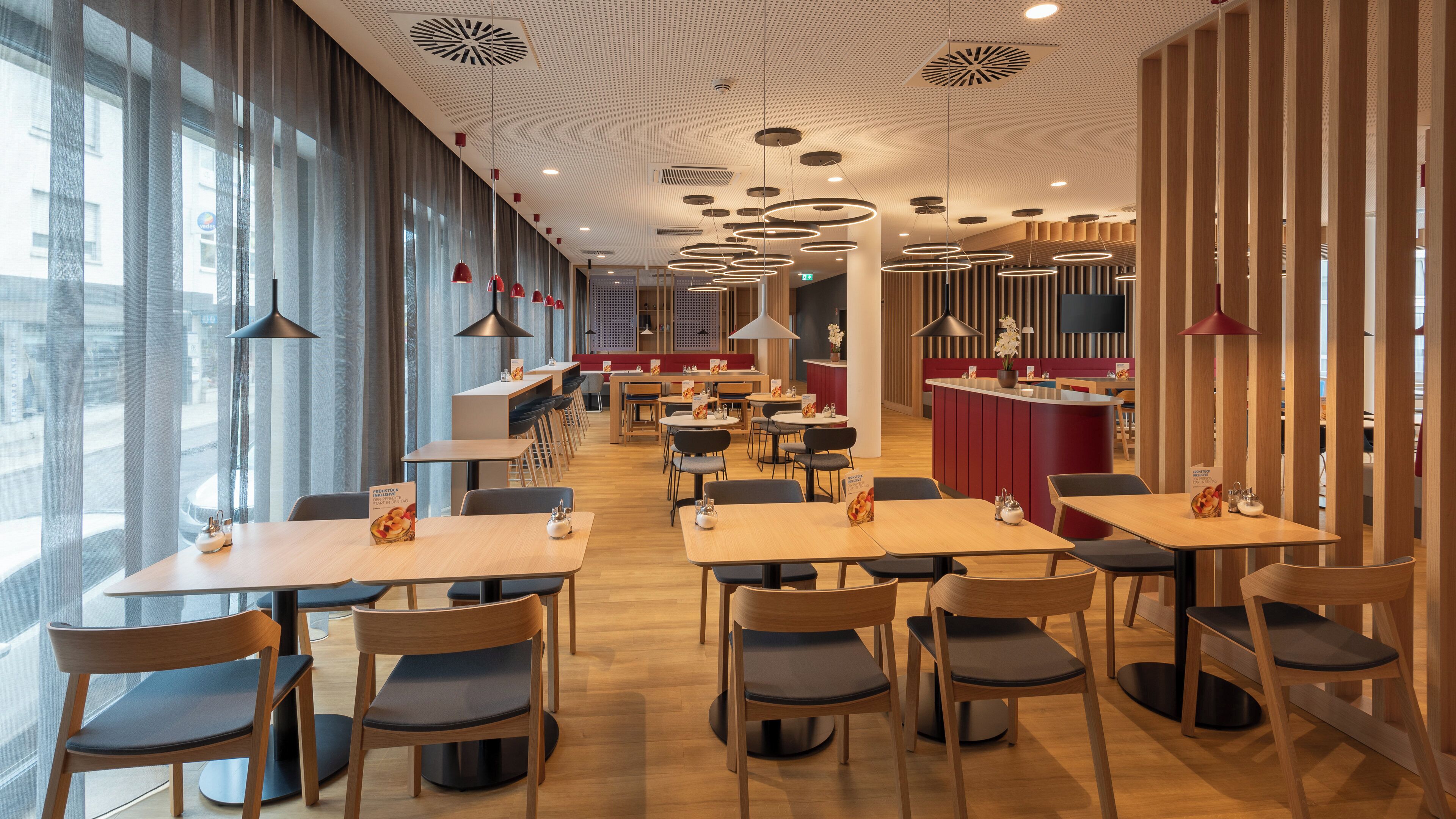 Ein modernes Restaurant mit Holztischen und -stühlen, einer Bar und großen Fenstern mit Blick auf die Stadt.